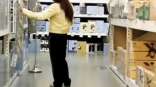 Dame in a yellow top and black pants is followed around and recorded in a store.